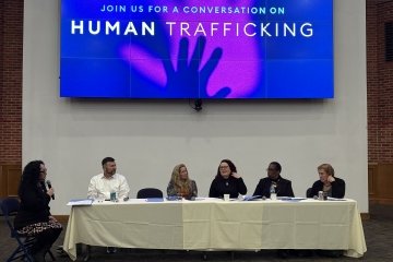 Moderator and guest panelists seated behind table at the front of the room for a human trafficking panel discussion at Mercy University